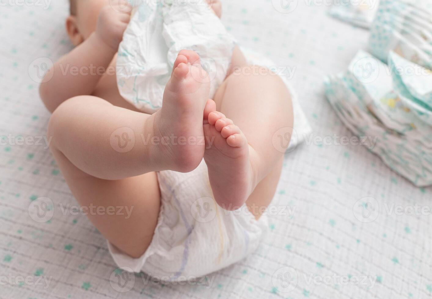 A baby in a diaper lies on a white background plays with a stack of diapers. Copy space for text photo