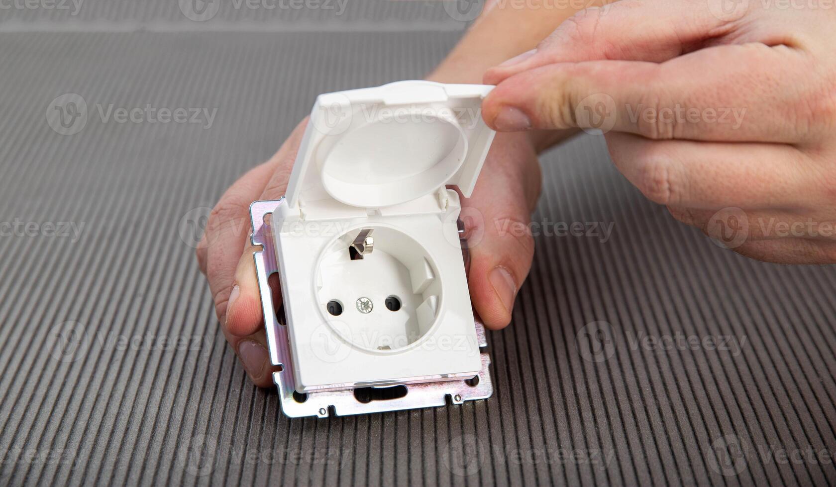A man's hand holds an electric switch with a protective cover on a gray background, close-up. Splash and rain resistant outdoor socket, close-up photo