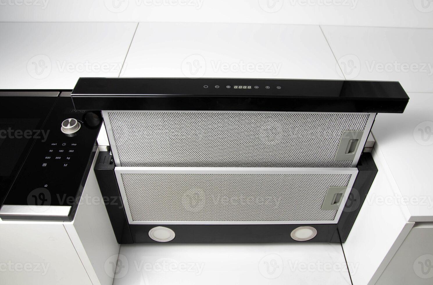 A modern black cooker hood in a white kitchen with a grease and charcoal filter. Air absorption photo