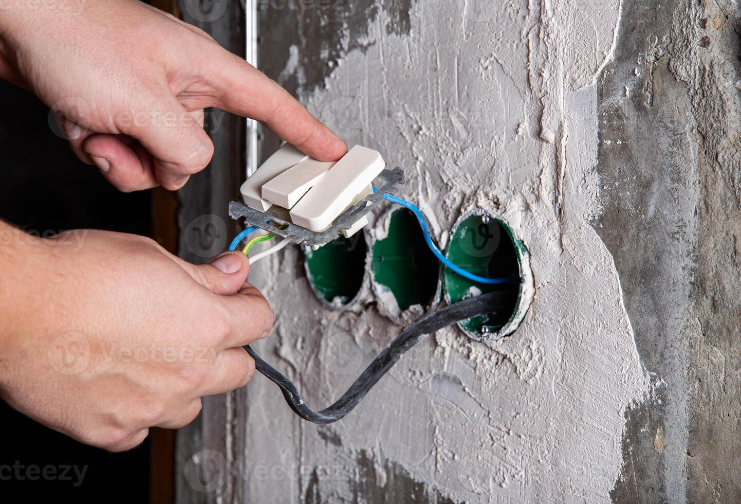 A man unsafely turns on the light on an electric switch and holds on to the wires. Danger of electric shock, close-up photo