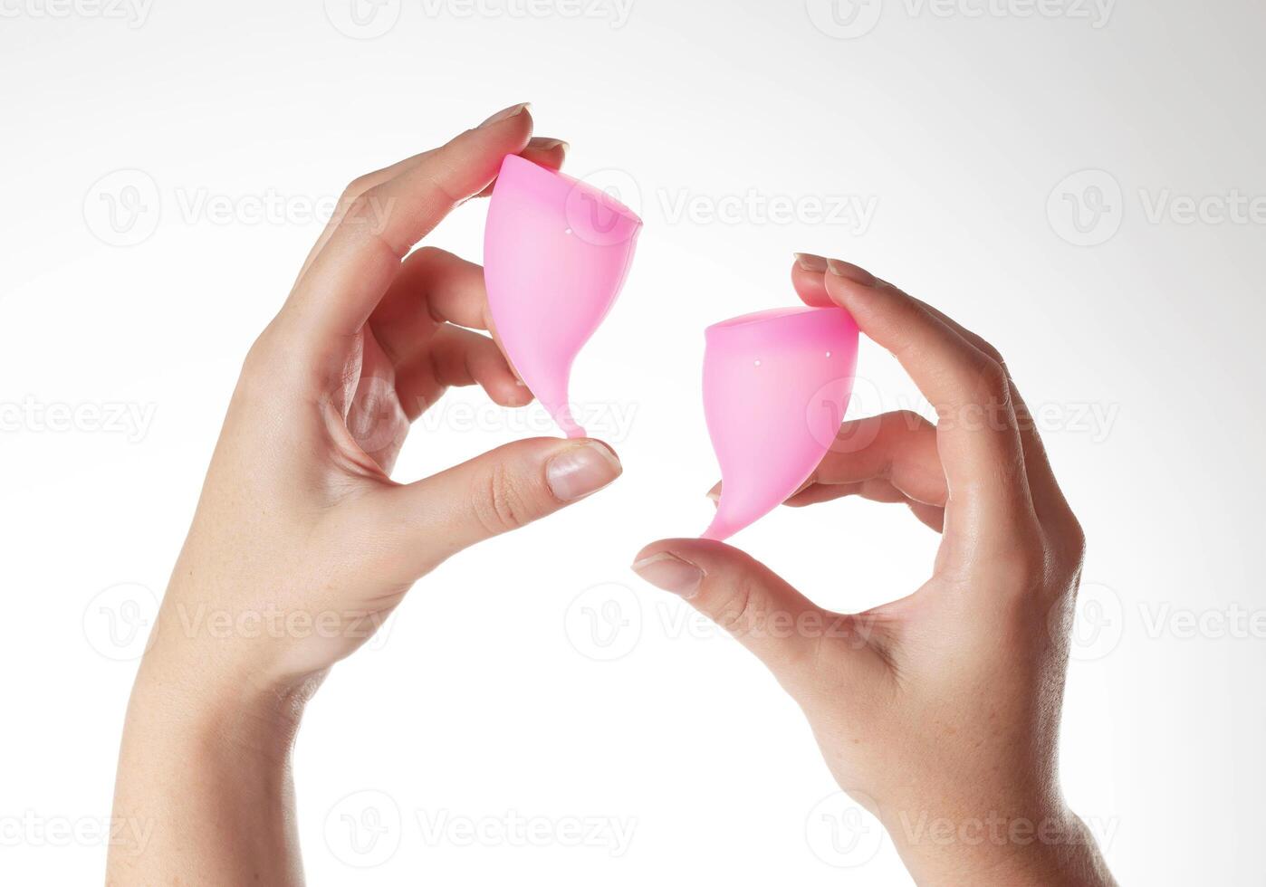 Female hands hold pink menstrual cups on a white background. Hygienic vaginal cups for collecting discharge during menstruation, close-up photo