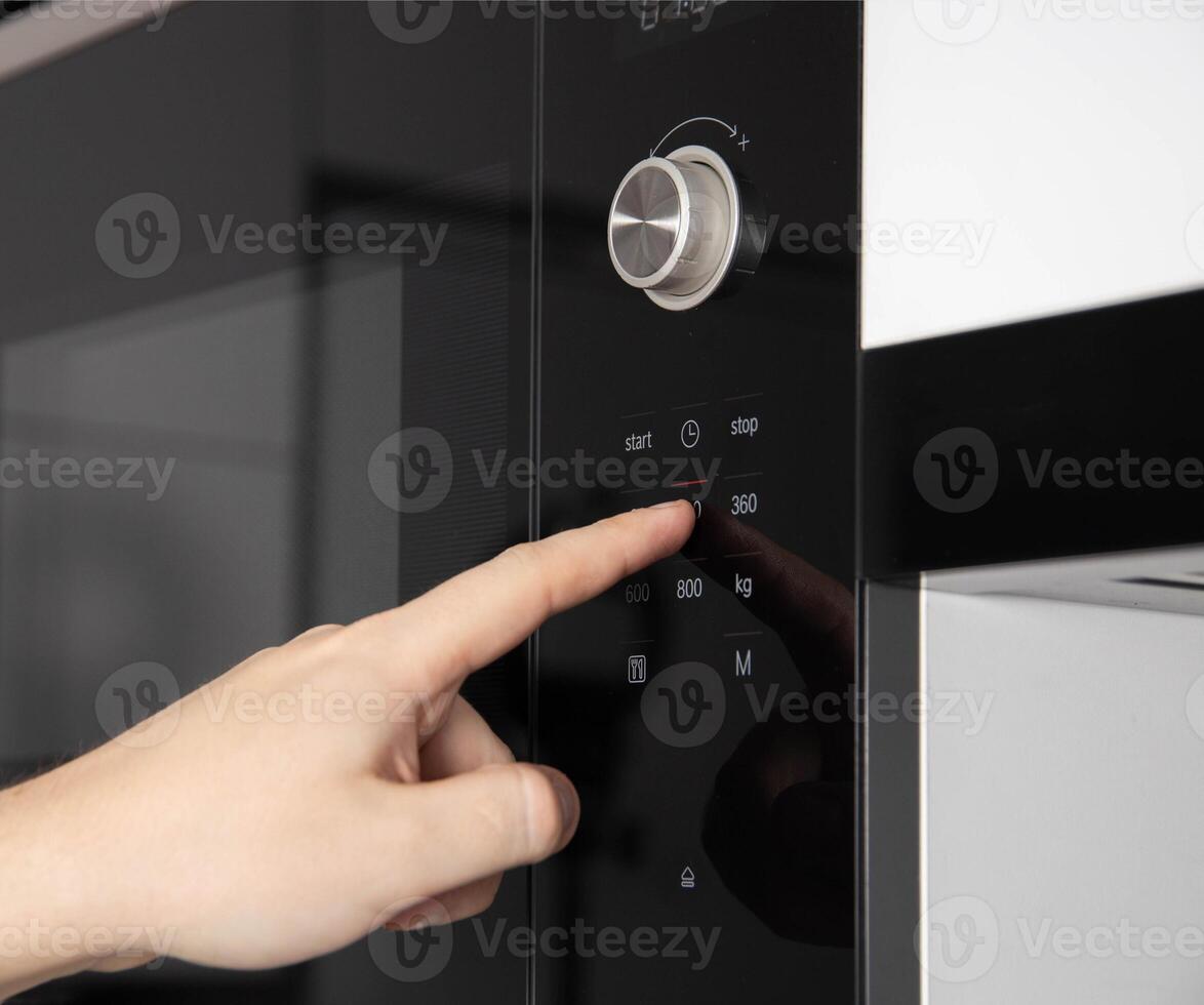 A man's hand presses the touch panel of a modern microwave oven to select the power and function of heating food. Close-up photo