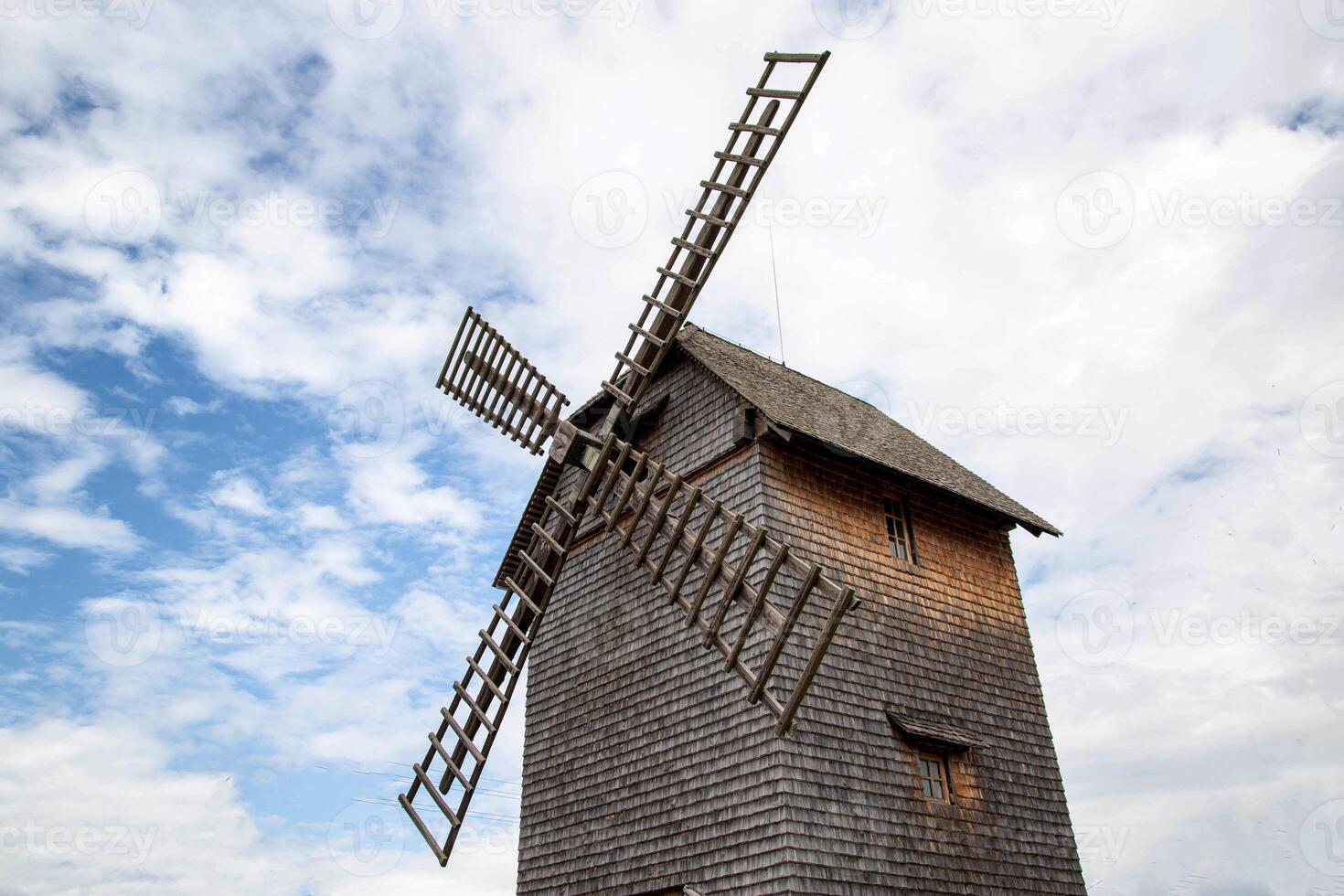 Beautiful old wooden mill in the village against the background of blue sky and clouds. Traditional, historical photo