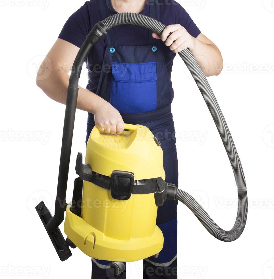 A man in overalls holds an industrial vacuum cleaner in his hands on a white background. The concept of cleaning services after renovation in the apartment. Cleaning of industrial premises, isolate photo