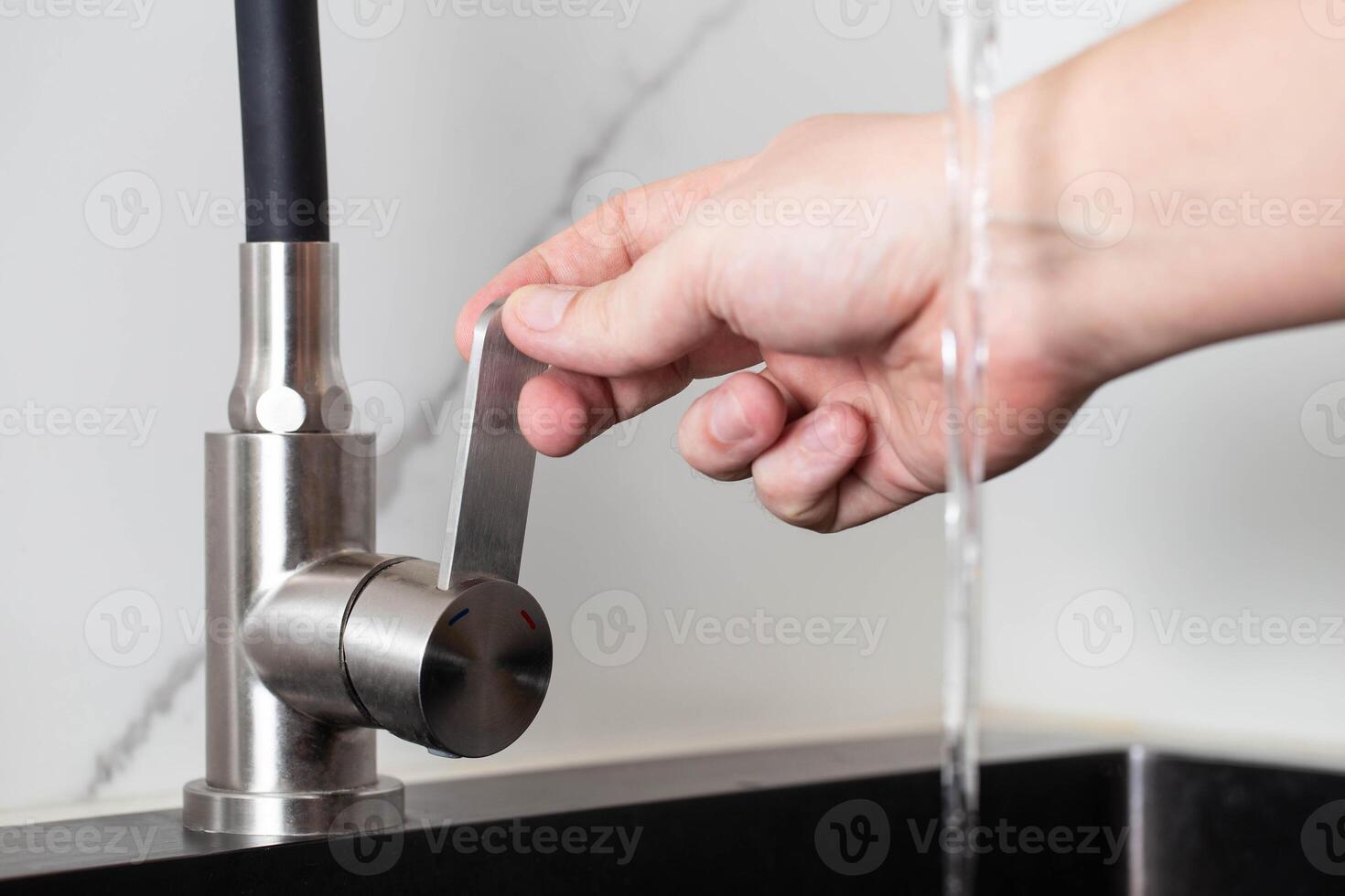 A man's hand regulates the power of the jet from a water tap. Cold and hot water, close-up. Quality faucet photo