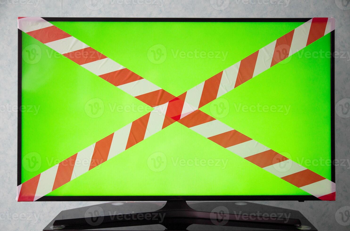Green TV screen with red and white prohibition tape. The concept of a sanction on television, a ban on broadcasting TV shows. Technology photo