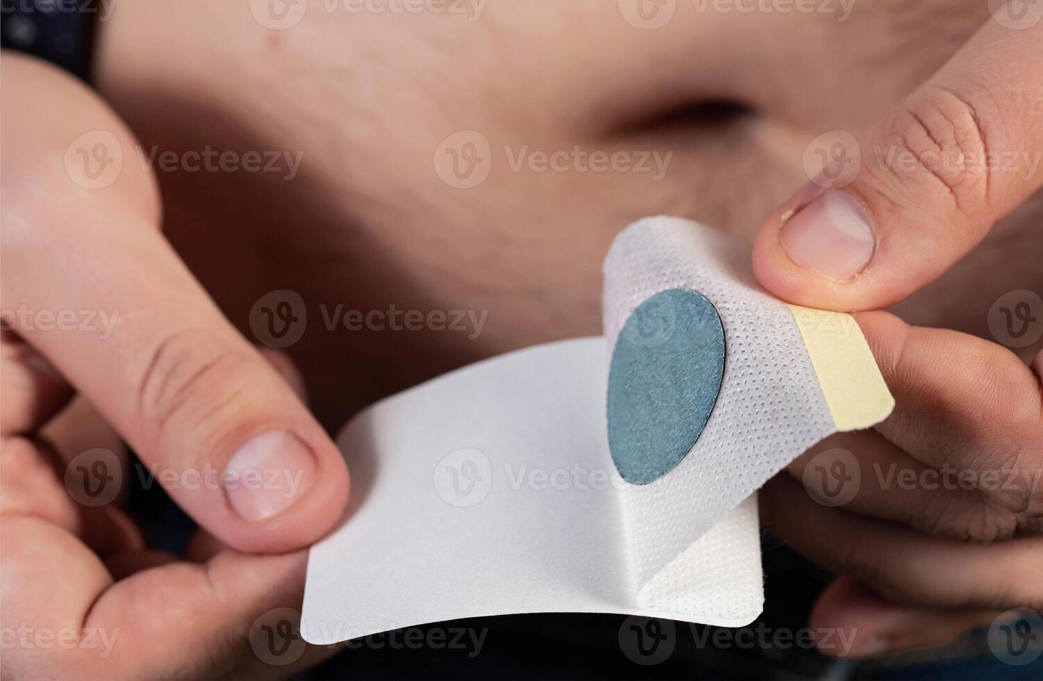 A modern medical patch for prostatitis and urinary tract infections. A man glues a urological patch on his stomach, close-up photo