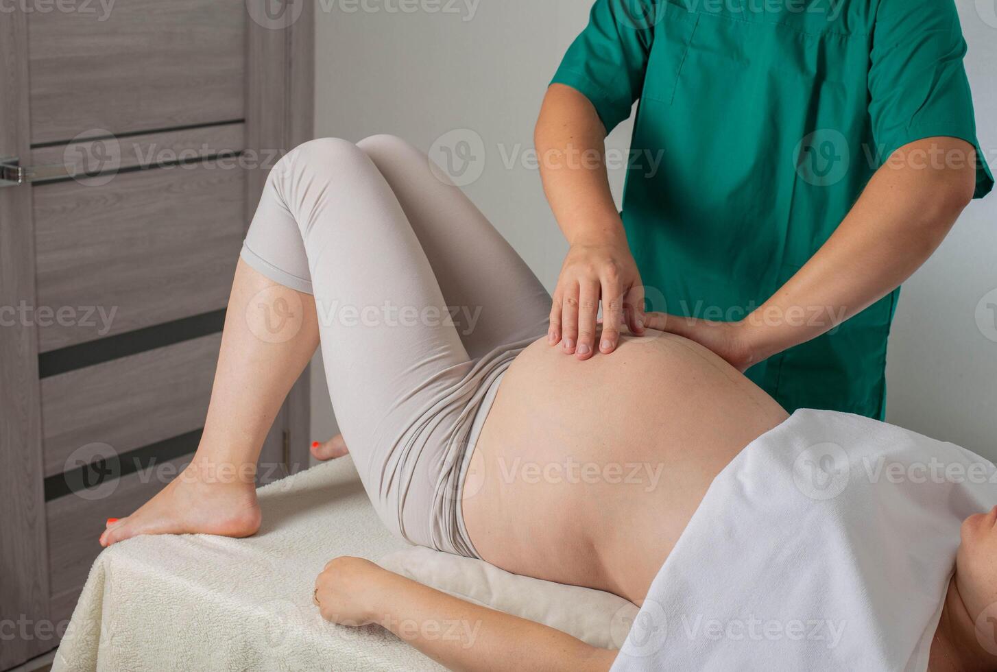 A chiropractic osteopathic doctor makes a massage to a pregnant girl in the 3rd trimester, background. Pregnant tummy photo