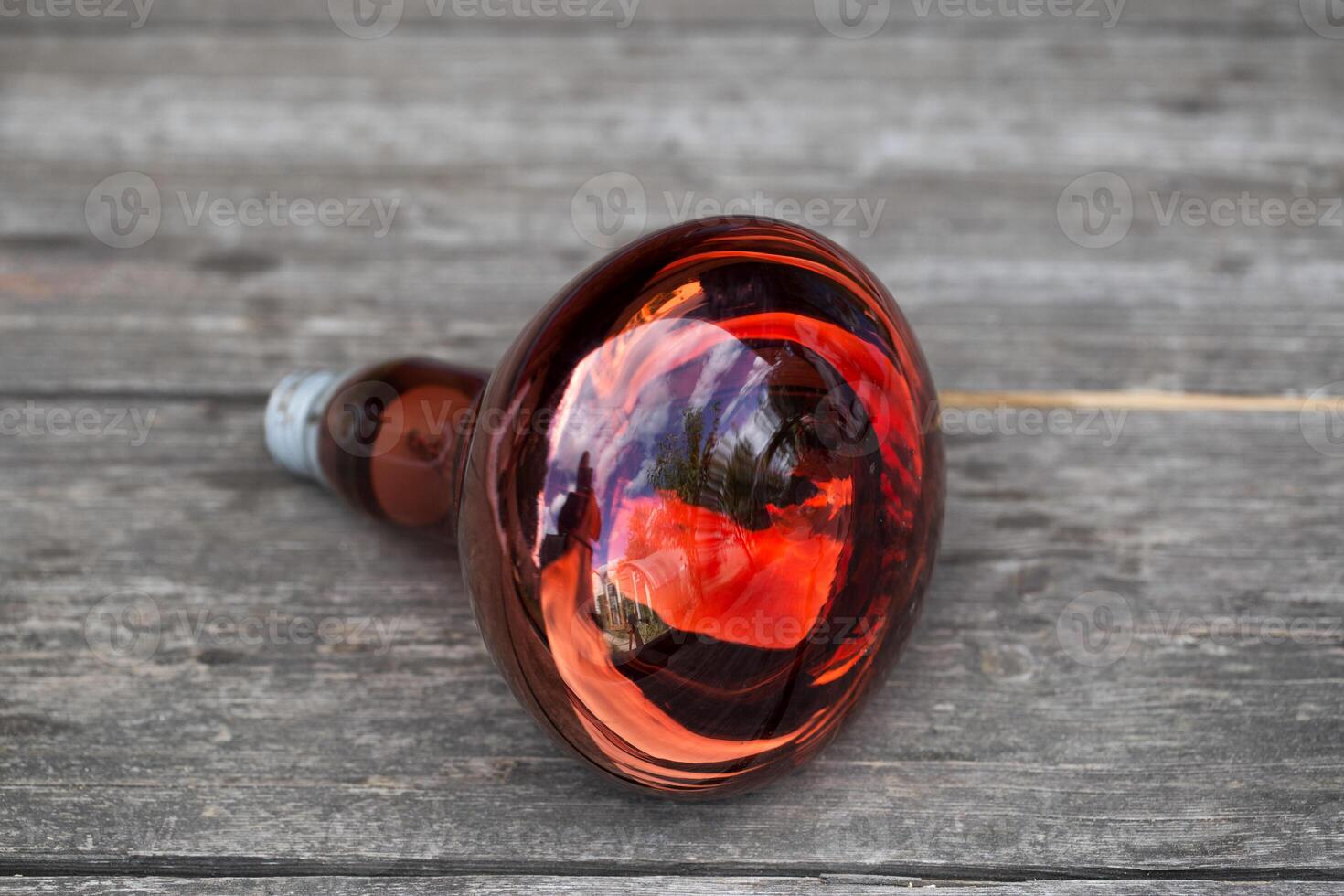 A red large lamp that radiates heat for animals and birds. Wooden background, close-up photo