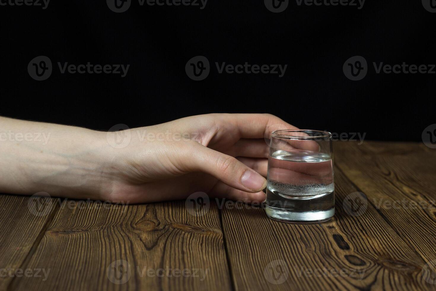 Female hand with alcohol in a glass on a wooden background, close-up, female alcoholism photo