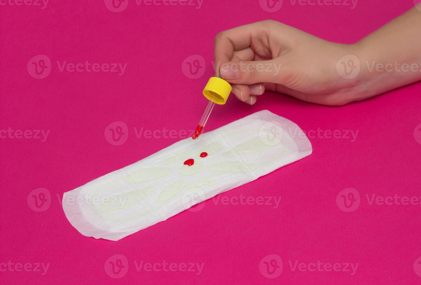 A girl is dripping drops of blood on the female gasket for menstruation in girls, the concept of critical days, pink background, close-up, copy space photo