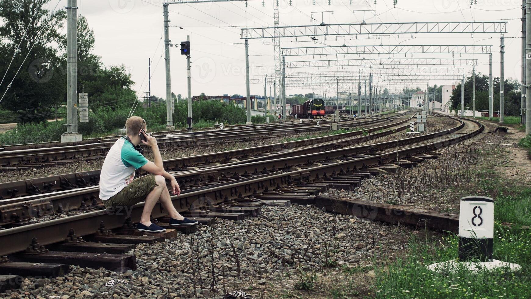 man is sitting on the railway or railroad and talkIng on the smartphone, life threatening photo