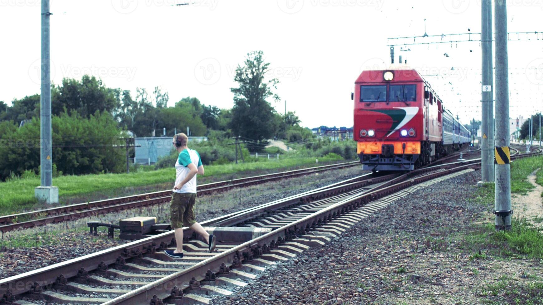 A caucasian man in headphones listens to music and crosses the railway right under the train, danger on the railway photo