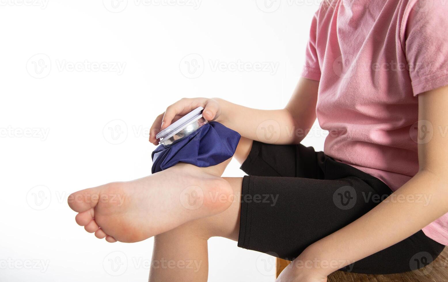 A girl applies a blue medical bag with ice to her ankle joint for a bruise on her leg. Local cryotherapy. Pain relief with cold, close-up. Copy space for text, compress bag photo