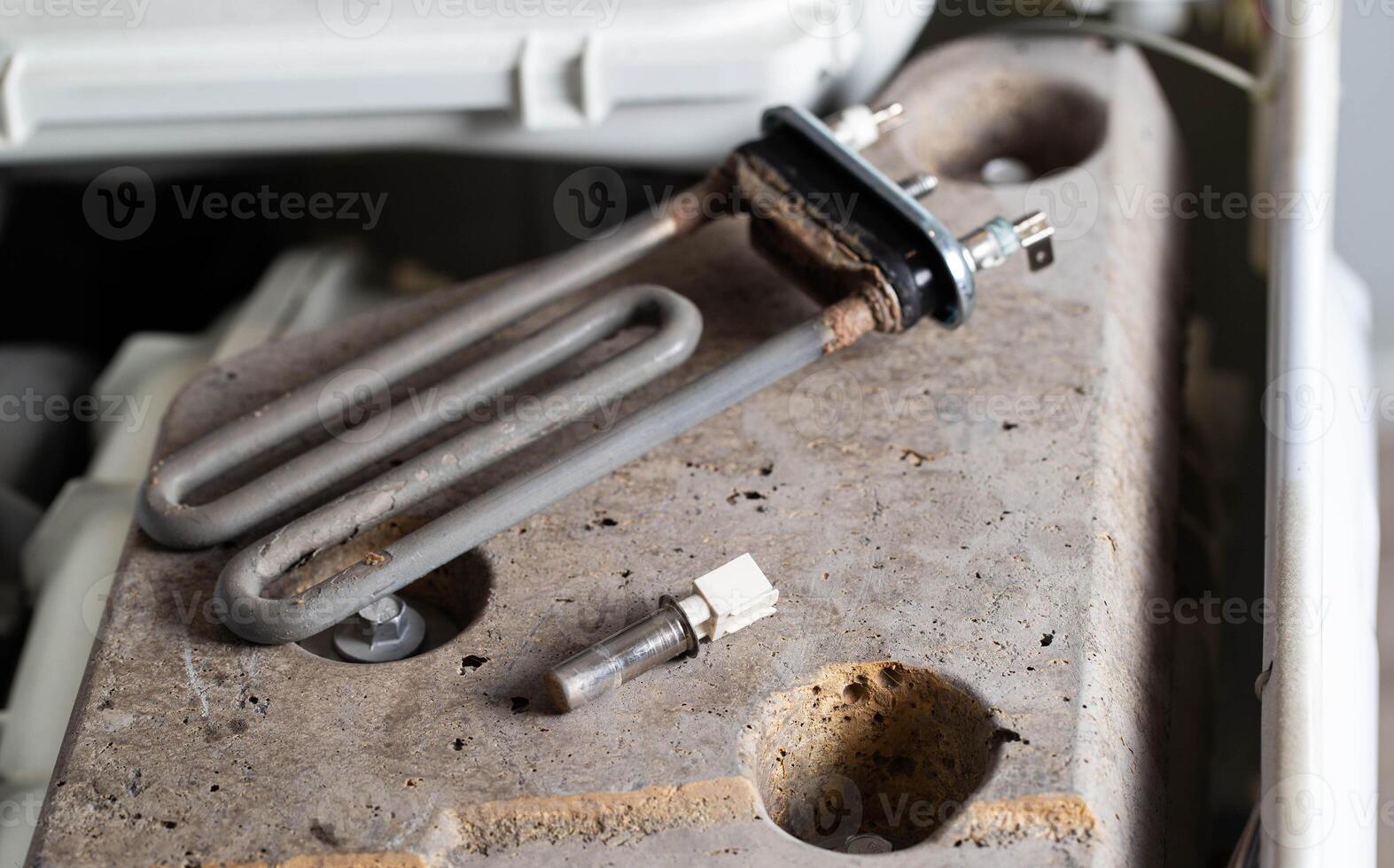 The electric heating element and temperature sensor, thermostat are on the disassembled washing machine. The concept of replacing and repairing spare parts in a washing machine. photo