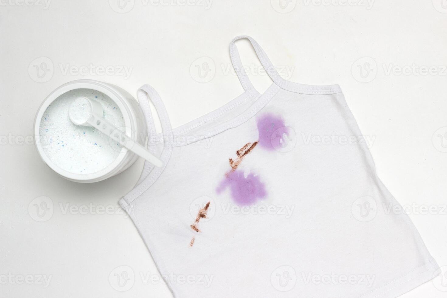 Children's white T-shirt with spots, next to the container with stain remover, close-up, white background photo