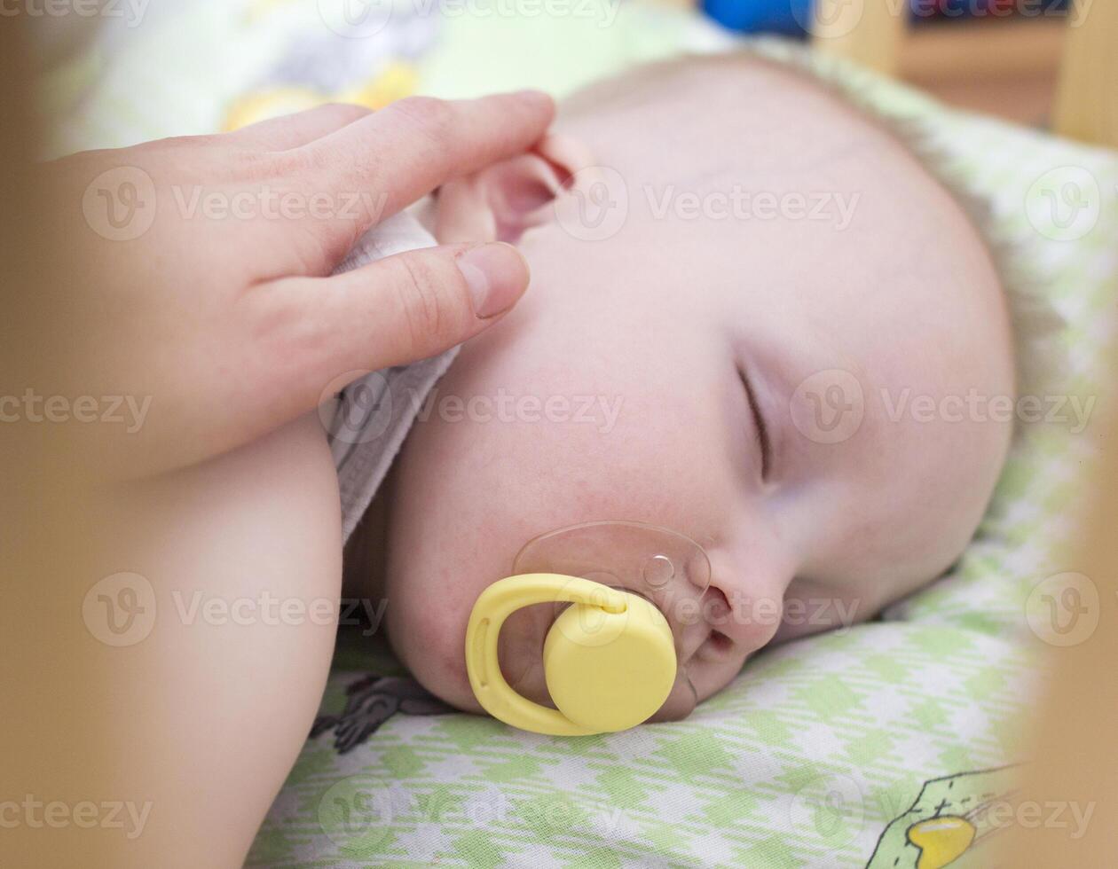 Mother stroking a sleeping baby with a pacifier photo
