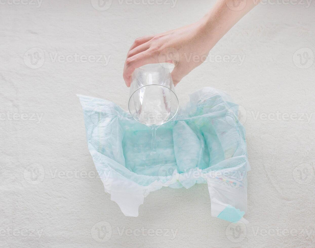 The girl pours a glass of water on a baby diaper, close-up photo