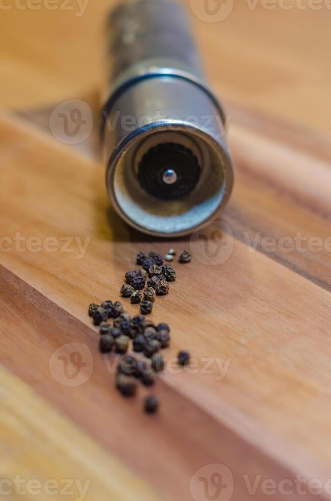 Pepper Grinder with Scattered Peppercorns on wooden background . High quality photo
