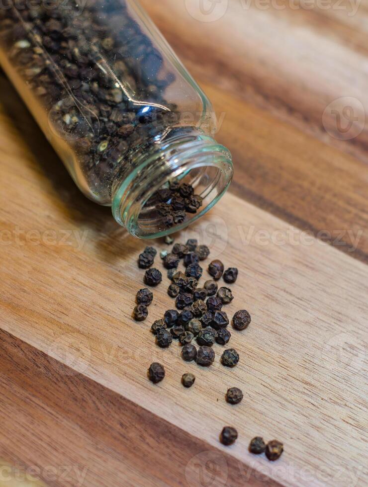 Black Peppercorns Spilled from a Glass Jar on wooden background. High quality photo
