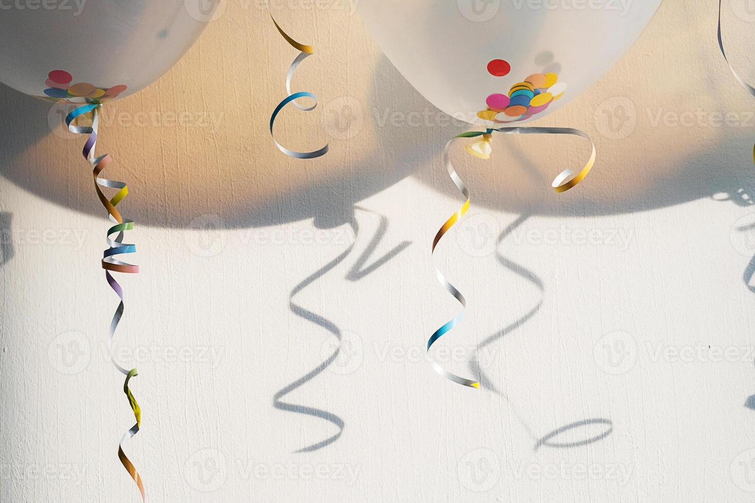 Balloons with colorful confetti and ribbons casting shadows on a wall. Celebration concept photo