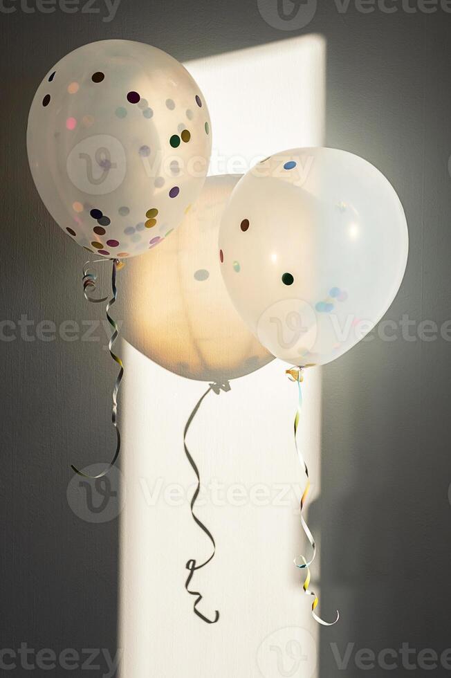 Two transparent balloons with colorful confetti, lit by sunlight and casting shadows. photo