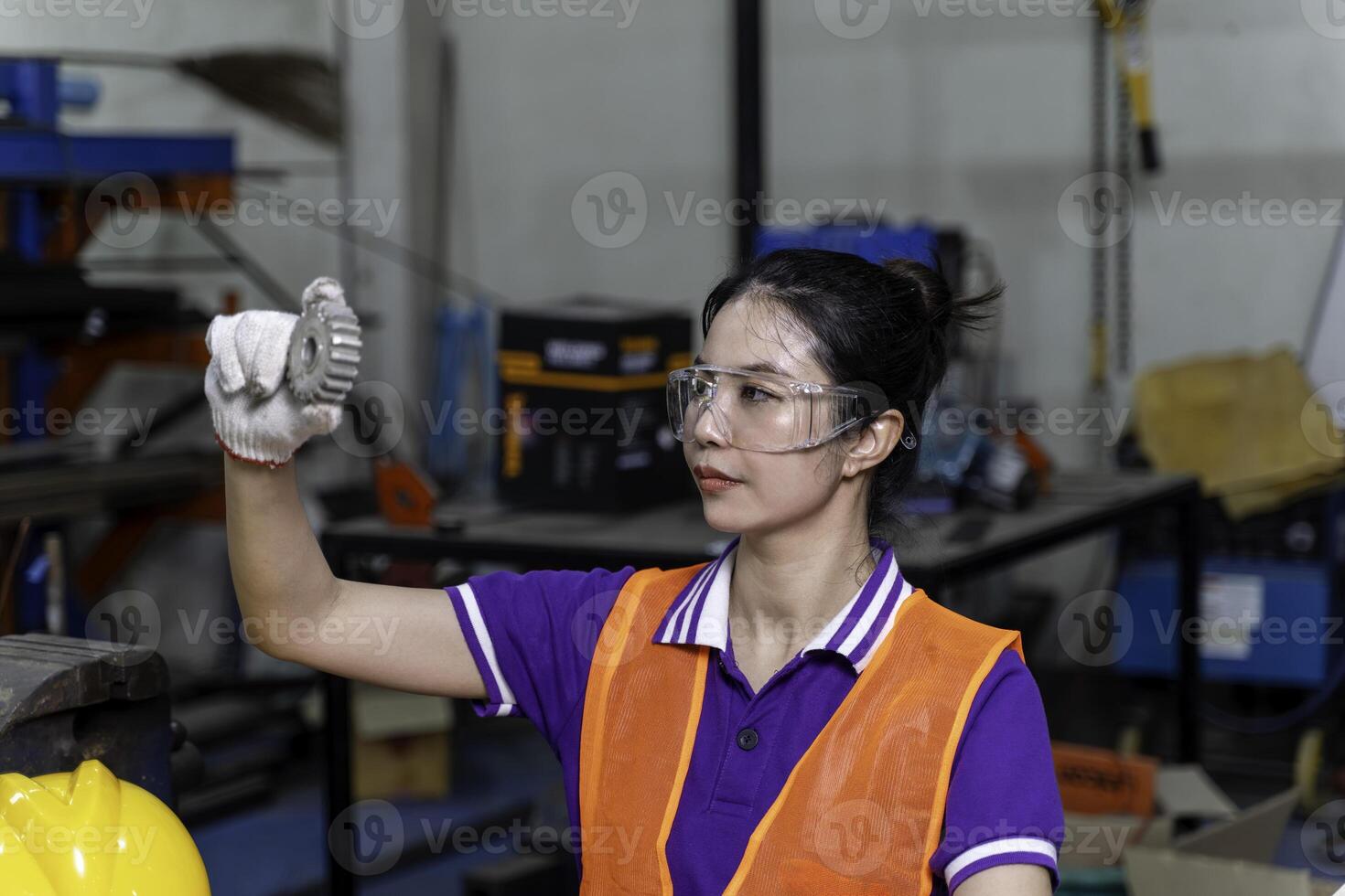 Closeup Asian woman industrial engineer looking an example small gear to check for completeness in industrial workshop. photo