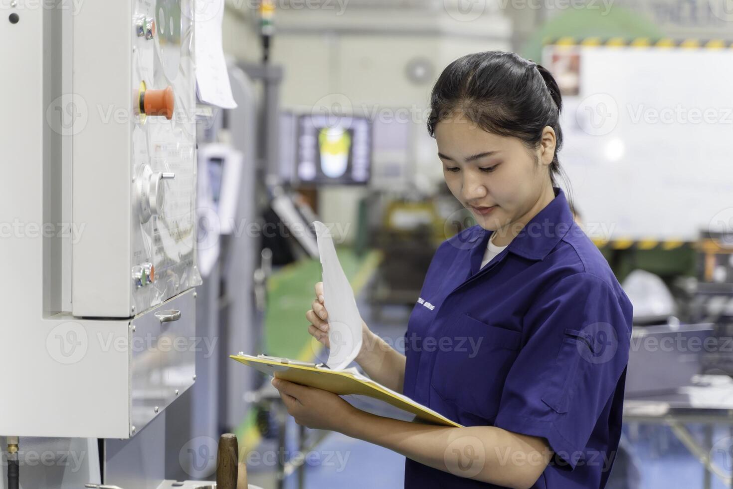 Asian woman industrial engineer wearing uniform checking of work list on clipboard with automated machinery in industrial workshop. photo