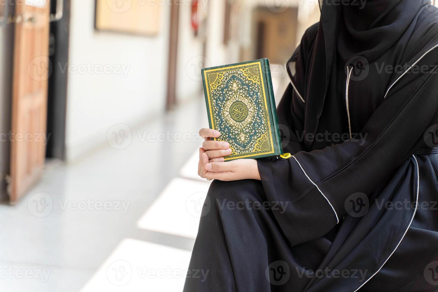 Closeup hands of Muslim students wearing traditional clothes holding Quran for reading during breaks time in university. Arabic texts is meaning Glorious Quran in English photo