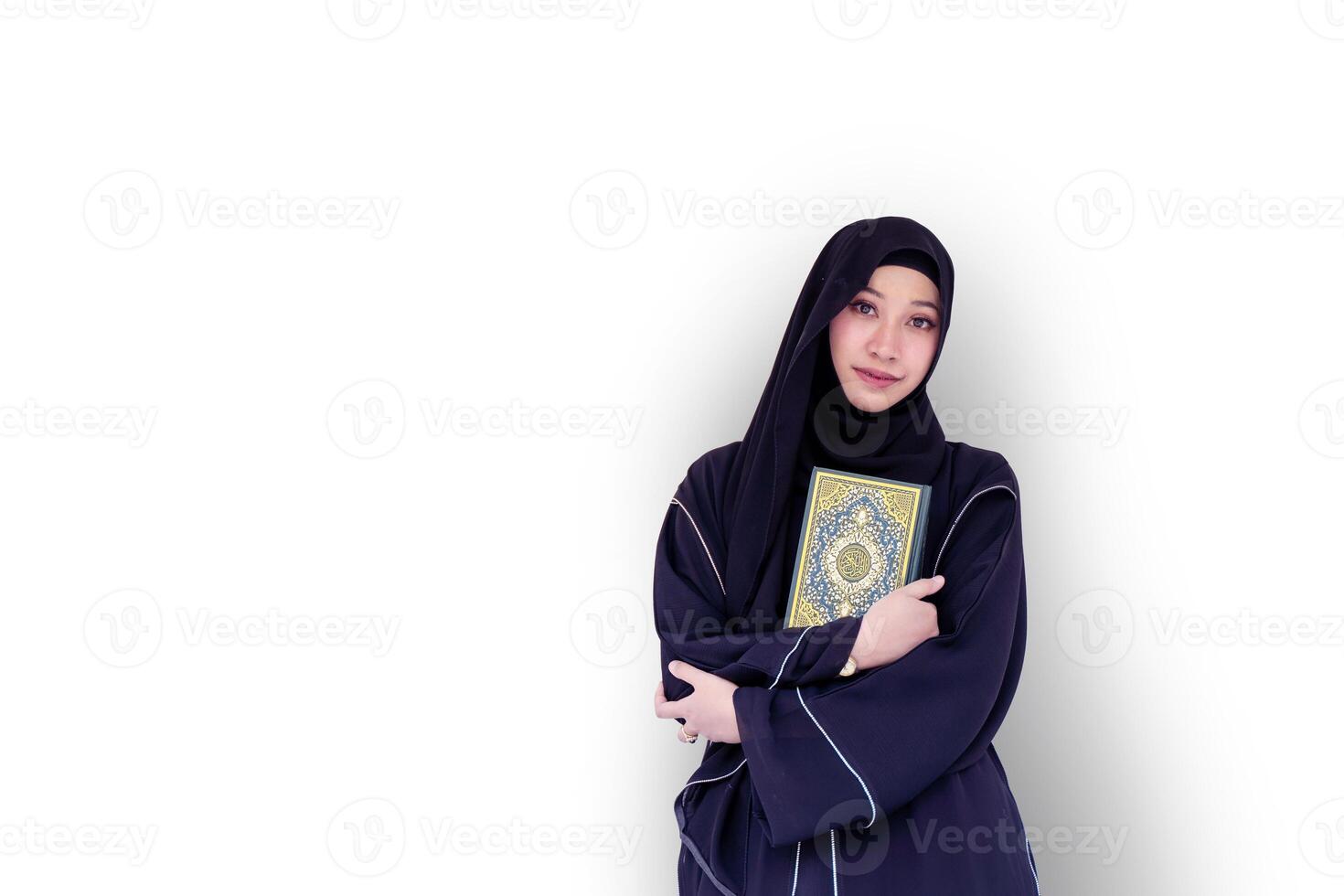 A beautiful Muslim student wearing abaya niqab traditional clothes portrait standing and hold Quran on white wall background. Arabic texts is meaning Glorious Quran in English. photo