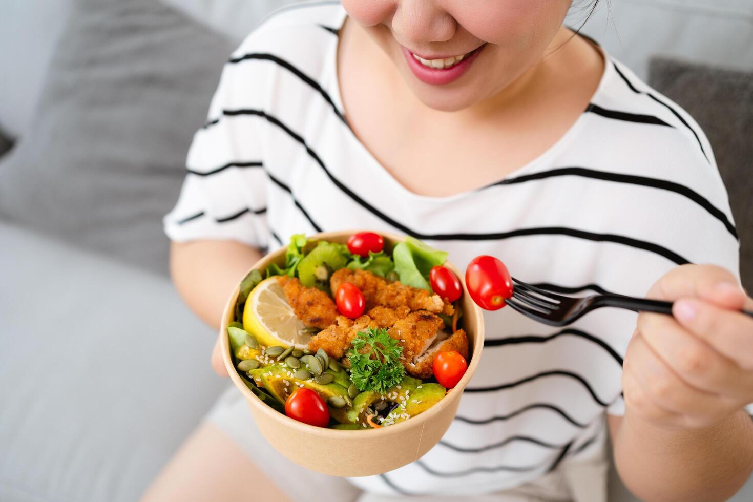 Beautiful Asian woman eating salad, holding a glass bowl and using a fork to pick up a tomato to eat photo