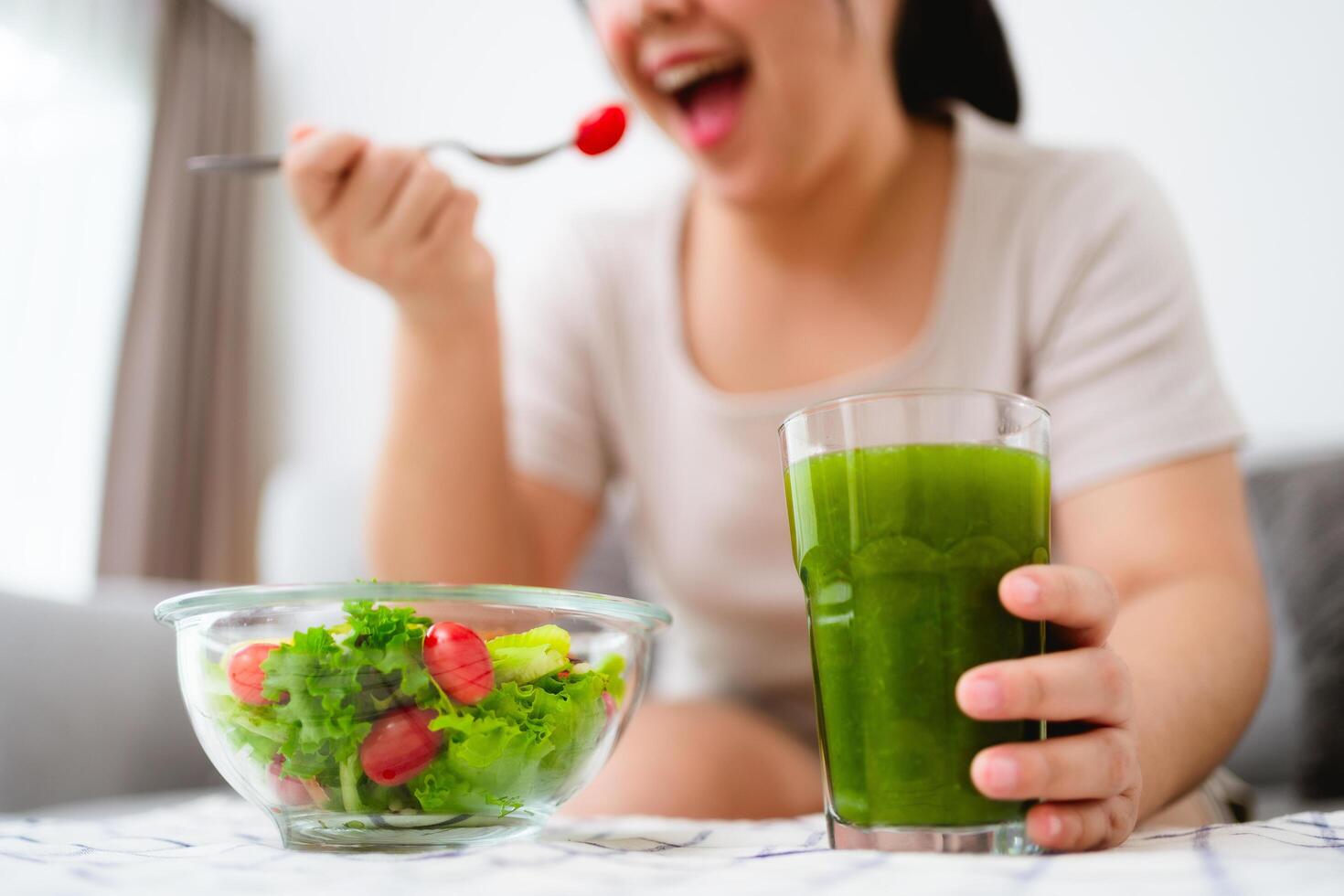 Beautiful Asian woman eating salad, holding a glass bowl and using a fork to pick up a tomato to eat photo