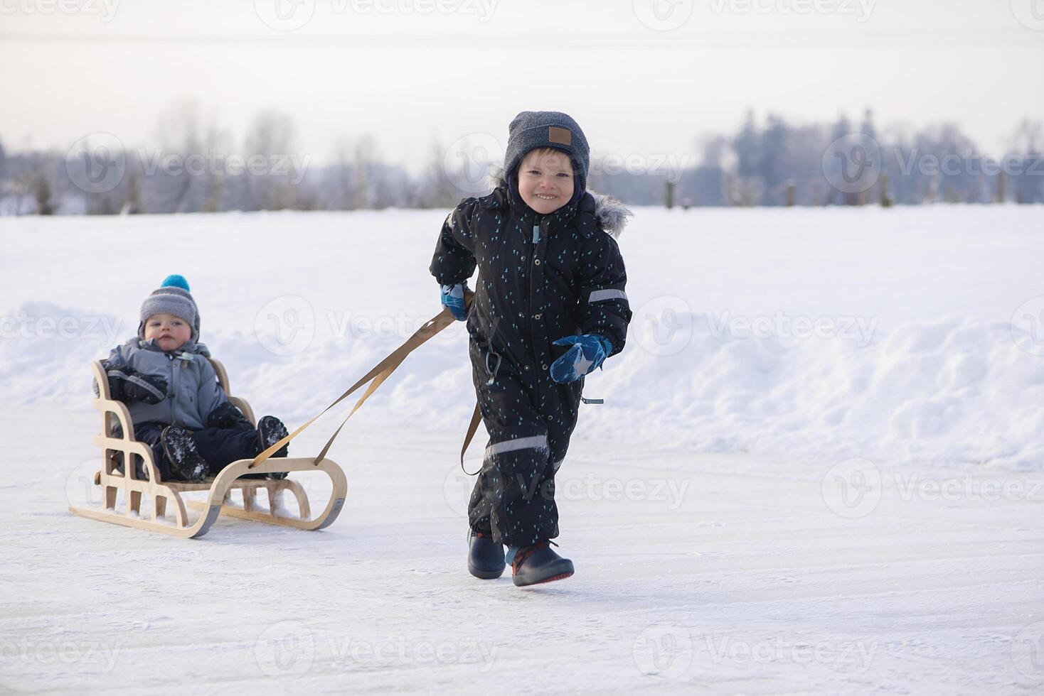 Happy children on a winter lake, playing together with a sledge while snowing photo