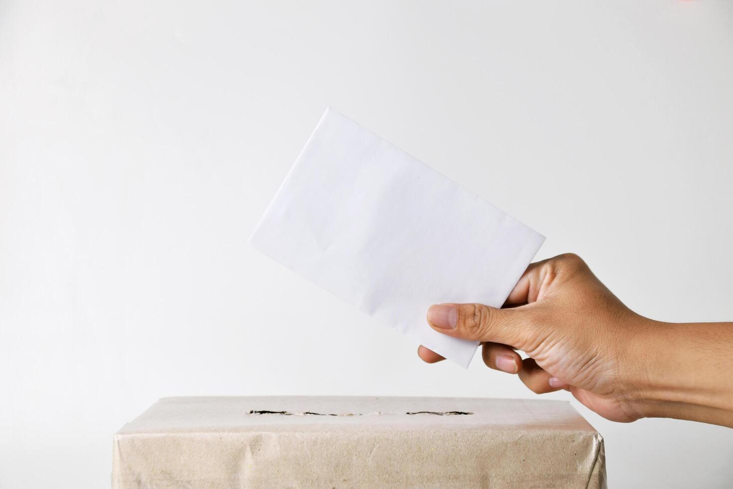 The voter's hand puts his or her vote into a cardboard ballot box photo