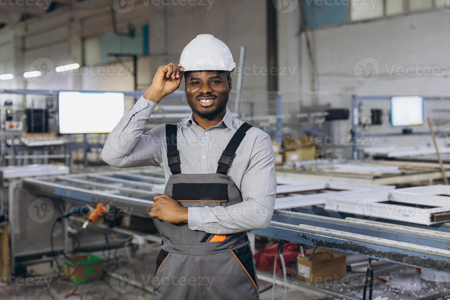 Smiling african american factory worker adjusting his hardhat in a window and door production line photo
