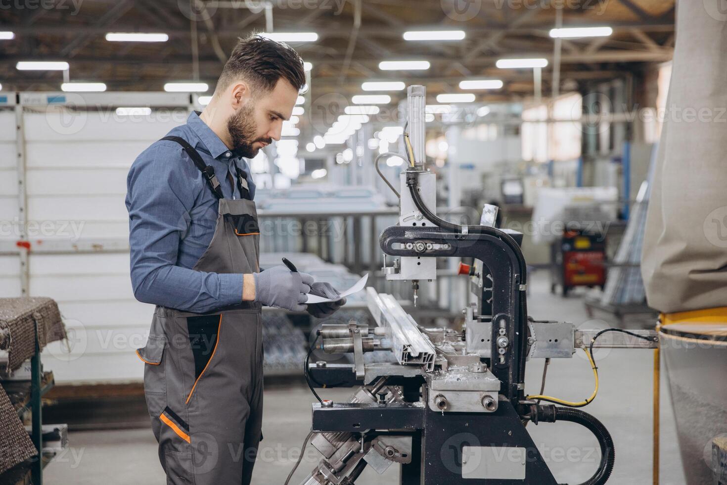 Factory worker taking notes while operating industrial machinery for aluminum window frames photo