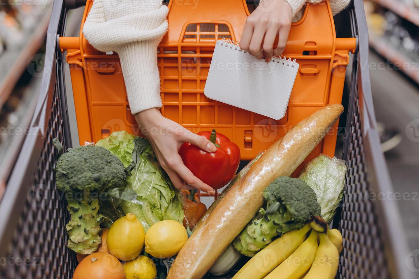 Woman grocery shopping with shopping list and fresh produce in basket photo