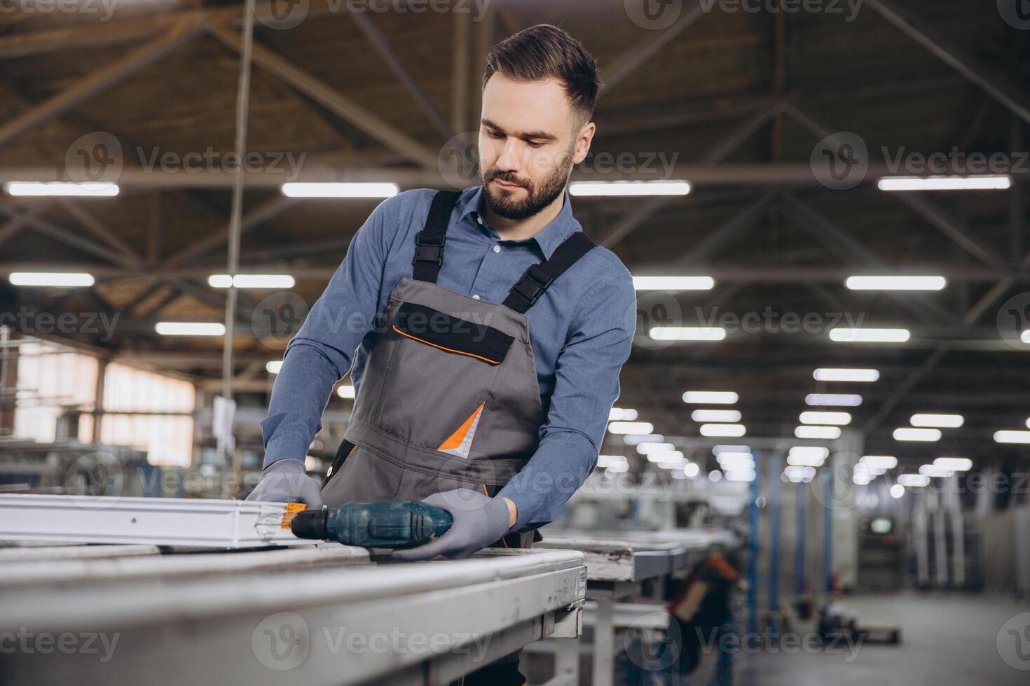 Factory worker assembling aluminum window frames using electric drill photo