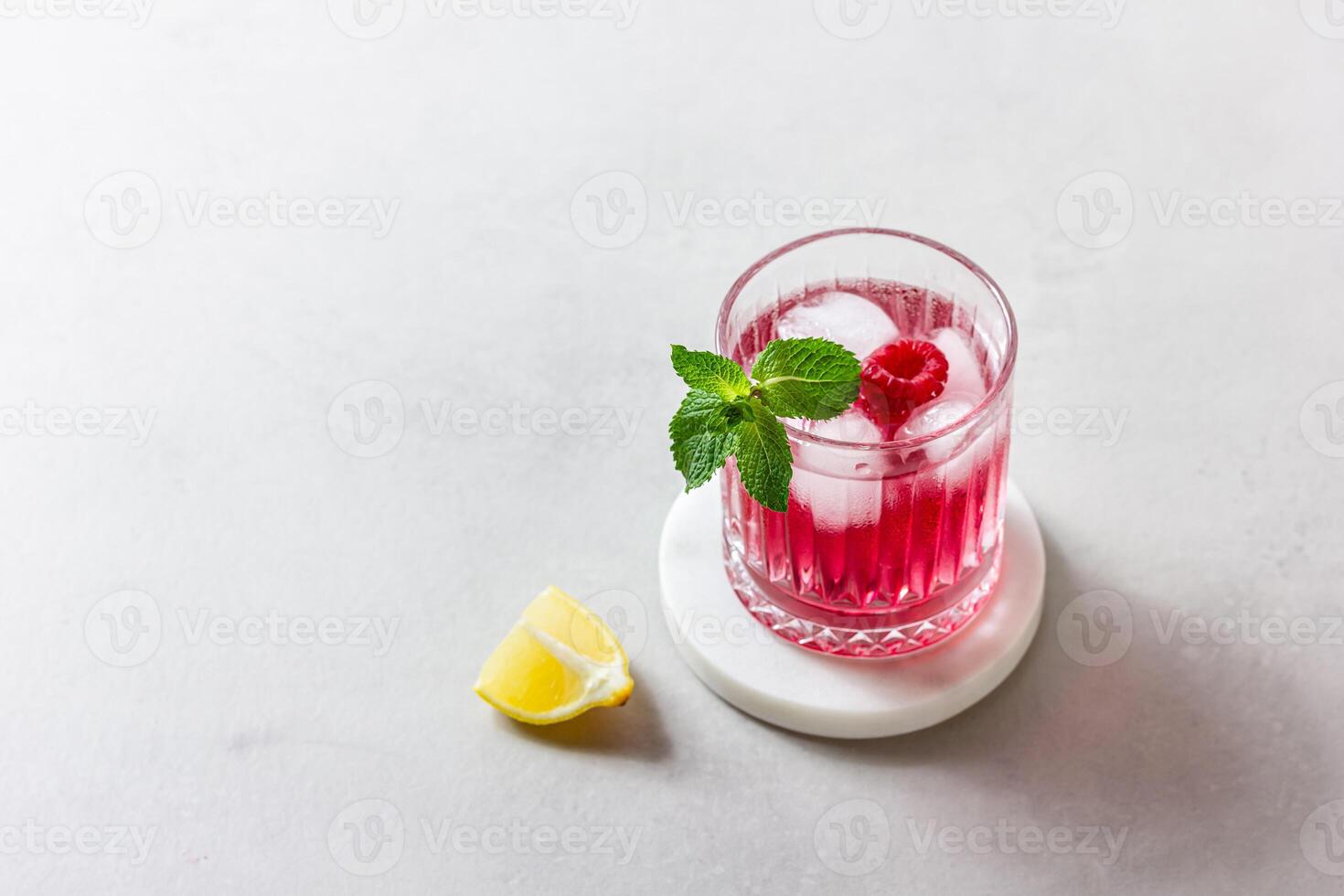 Raspberry cocktail with ice in a glass on a light background photo