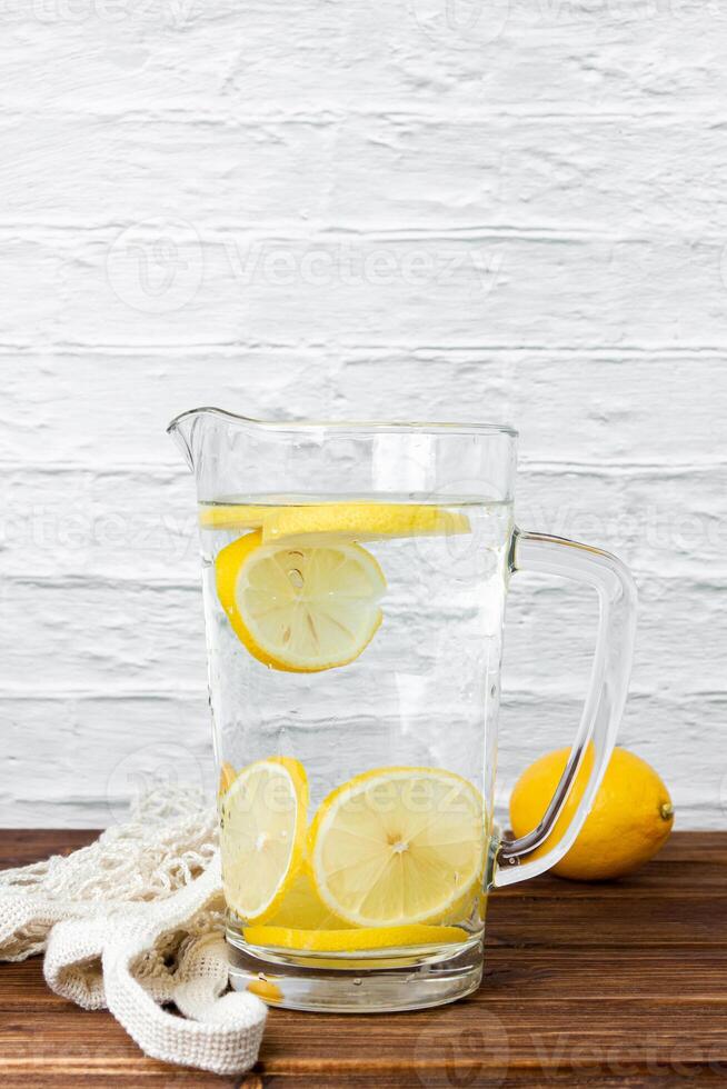 Water with lemons in jug on wooden table. photo