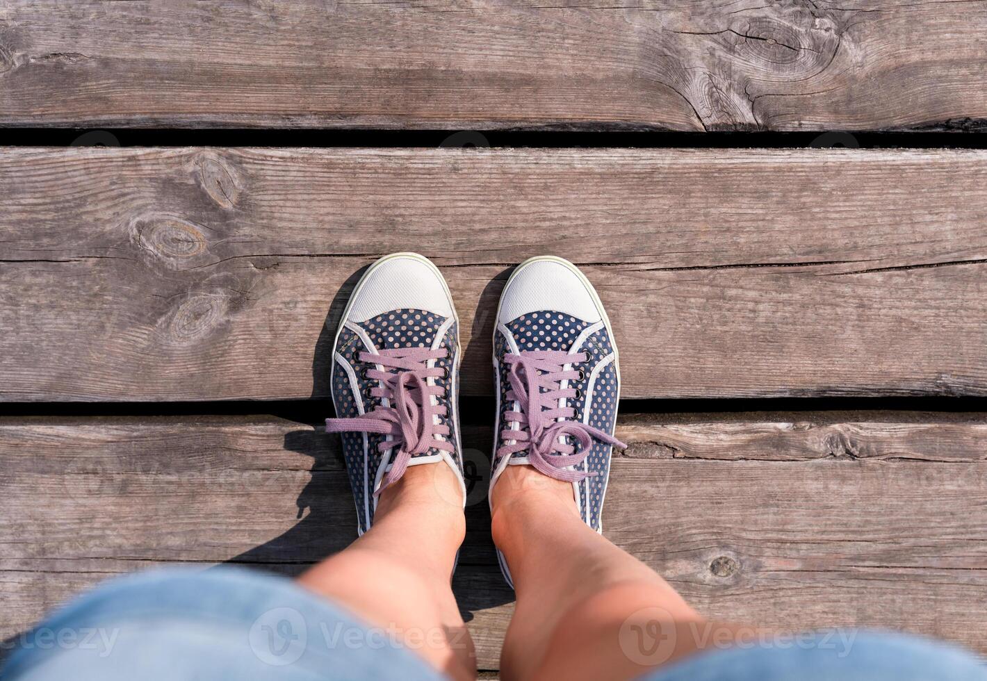 Female legs in polka dot sneakers on on a wooden pontoon. Top view. Copy space. photo