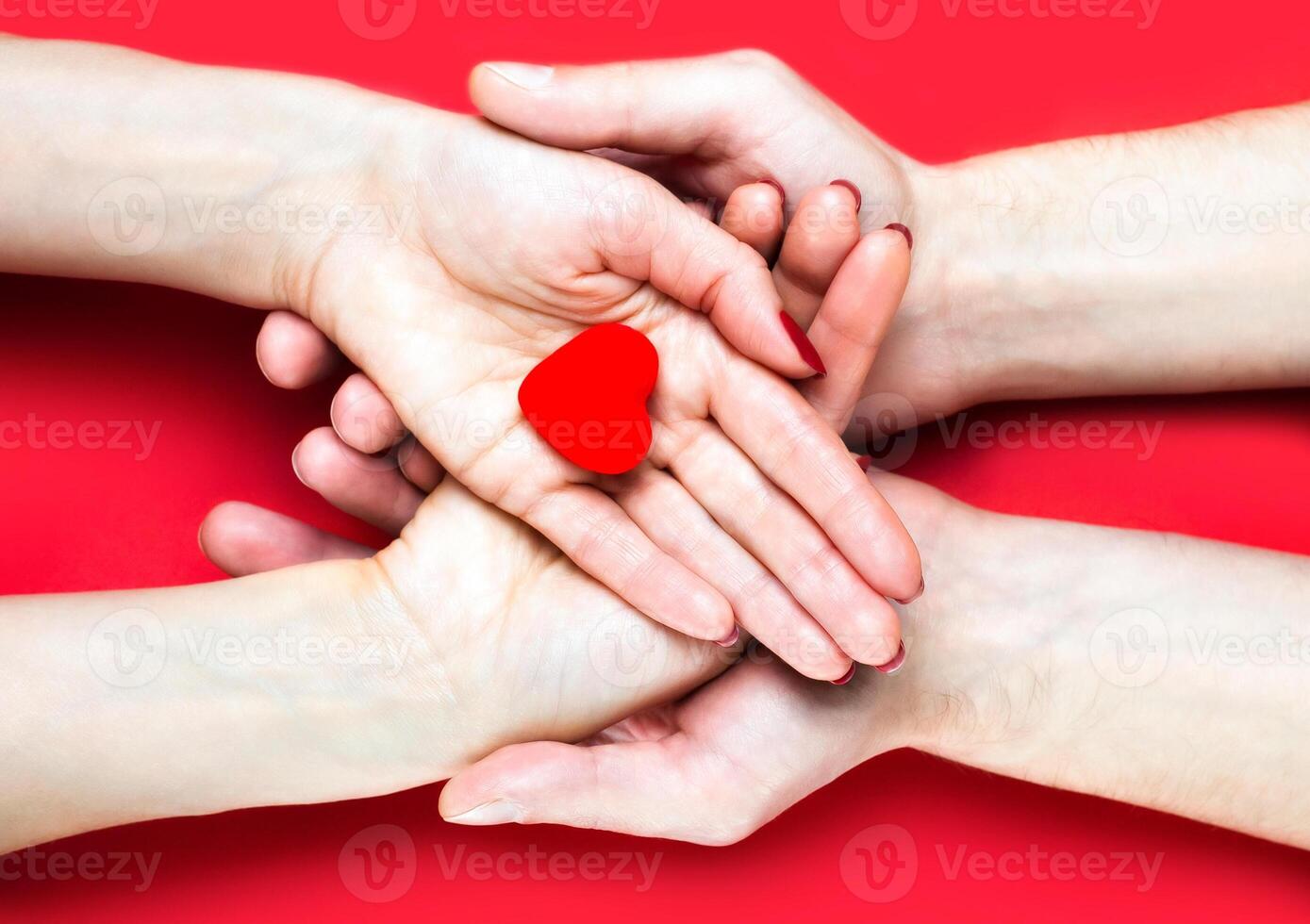 Females and males hands holds red heart on red background. Close-up. Top view. photo