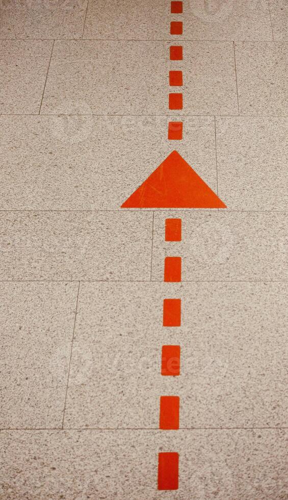 Orange Arrow and Dashed Line on Beige Tiled Floor photo