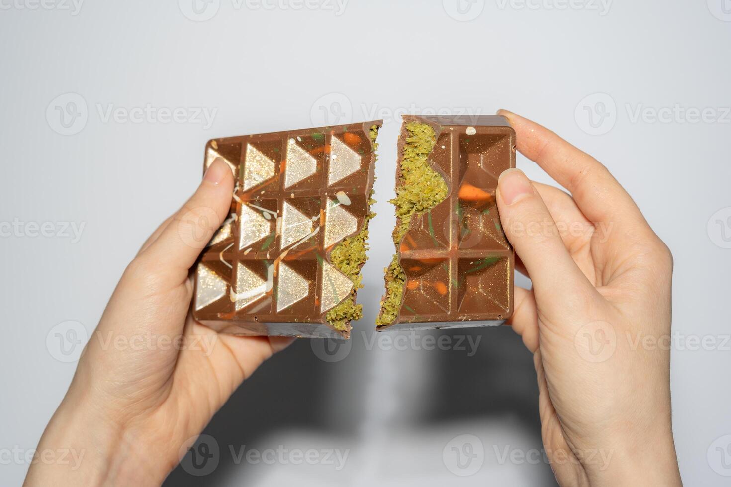 Trend Dubai chocolate with pistachio, tahini and kadaif broken in woman's hands. Confectionery handmade sweets, chocolatier photo