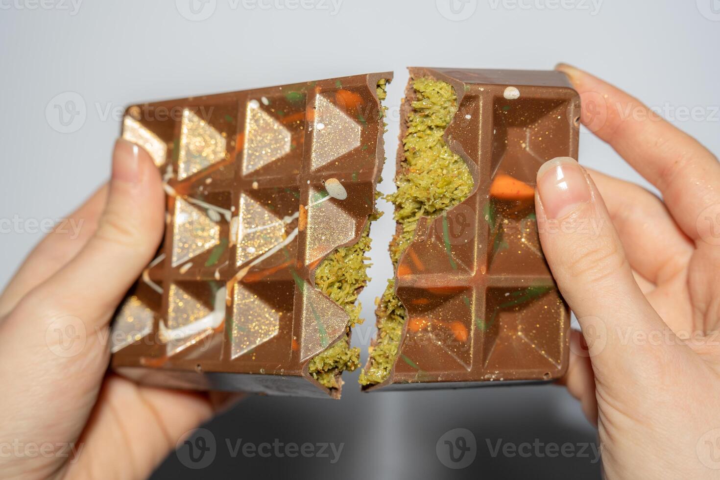 Close up of famous Dubai chocolate with pistachio, tahini and kadaif broken in woman's hands. Confectionery handmade sweets, chocolatier photo