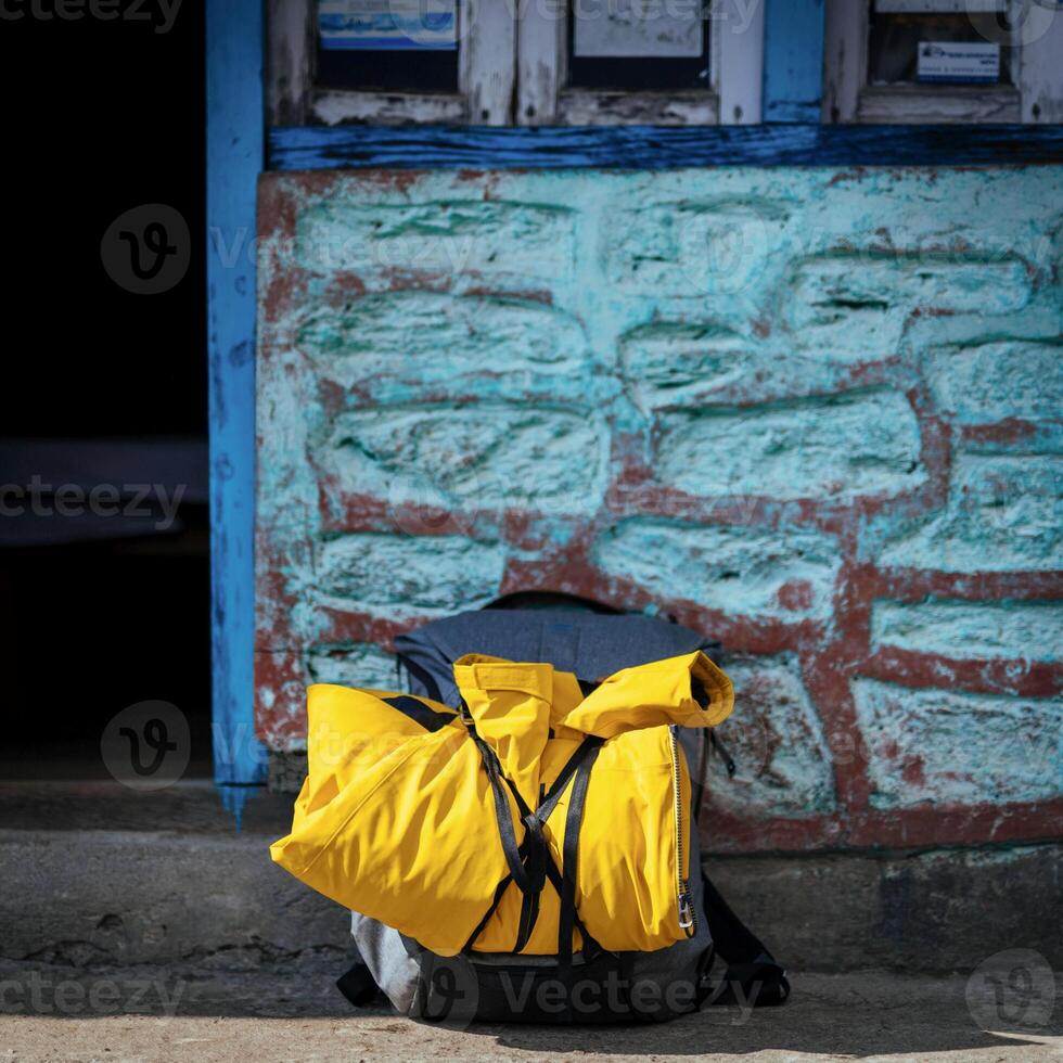 A yellow backpack rests quietly near a blue weathered wall. Concept of travel, exploration, and the essence of adventure. photo