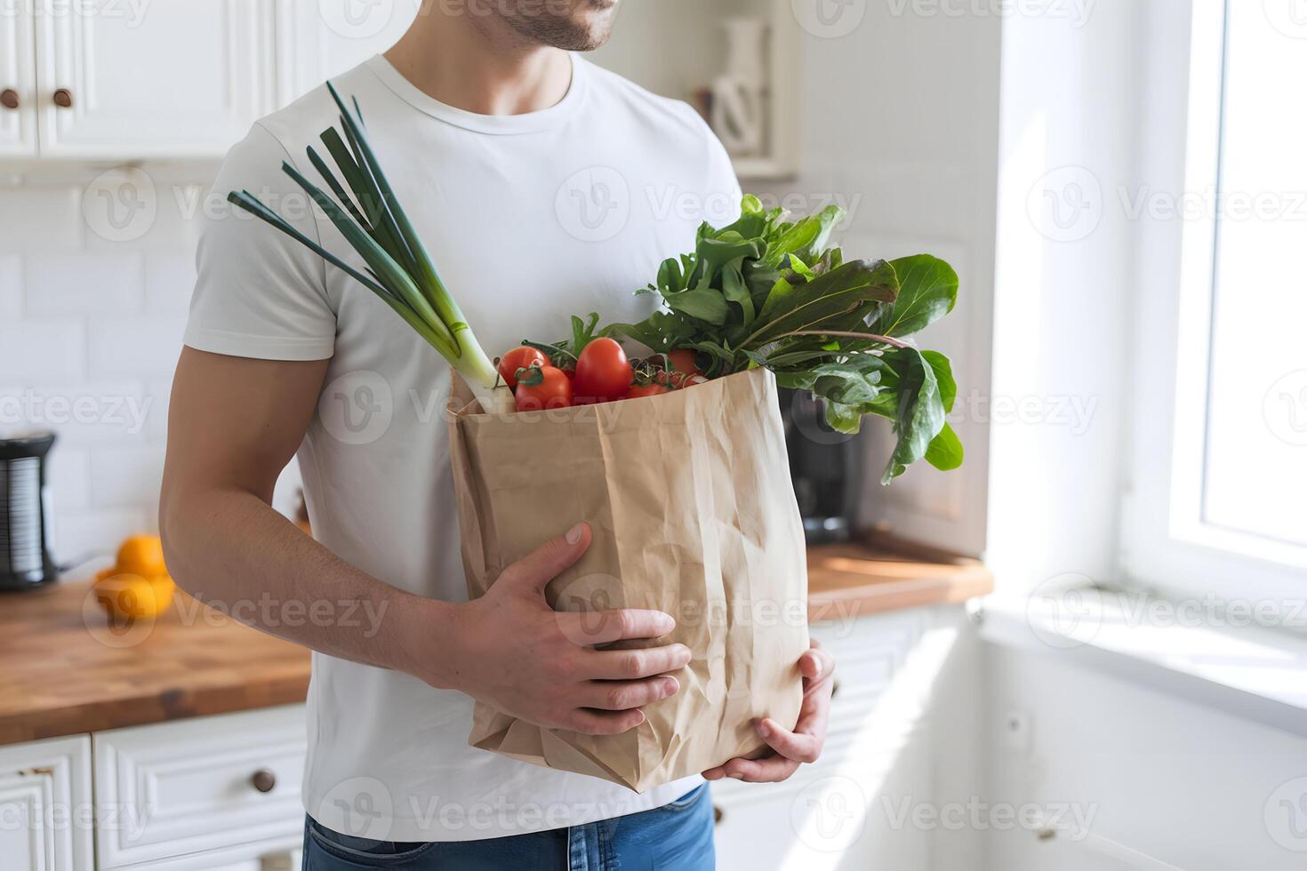 Man in bright kitchen holding paper bag of fresh vegetables, sunlight illuminates photo