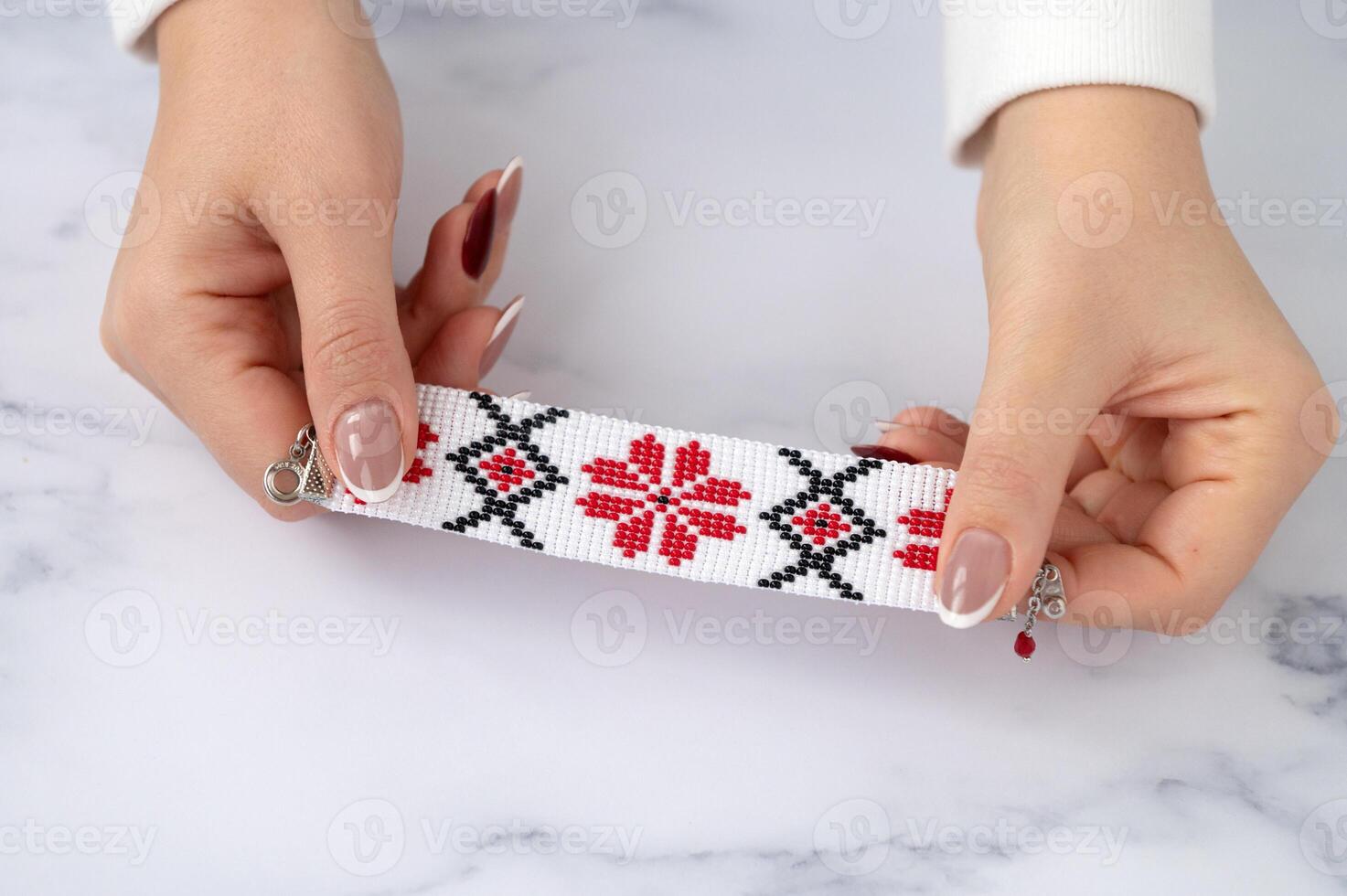 Caucasian female adult holding handmade red and black beaded bracelet on white surface photo