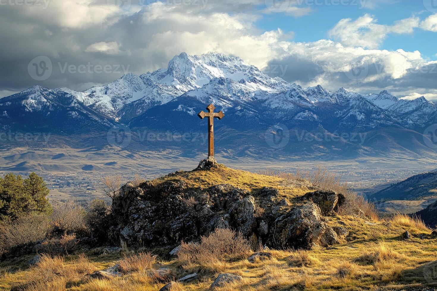 Large wooden cross standing on rocky hill overlooking snowy mountain range photo