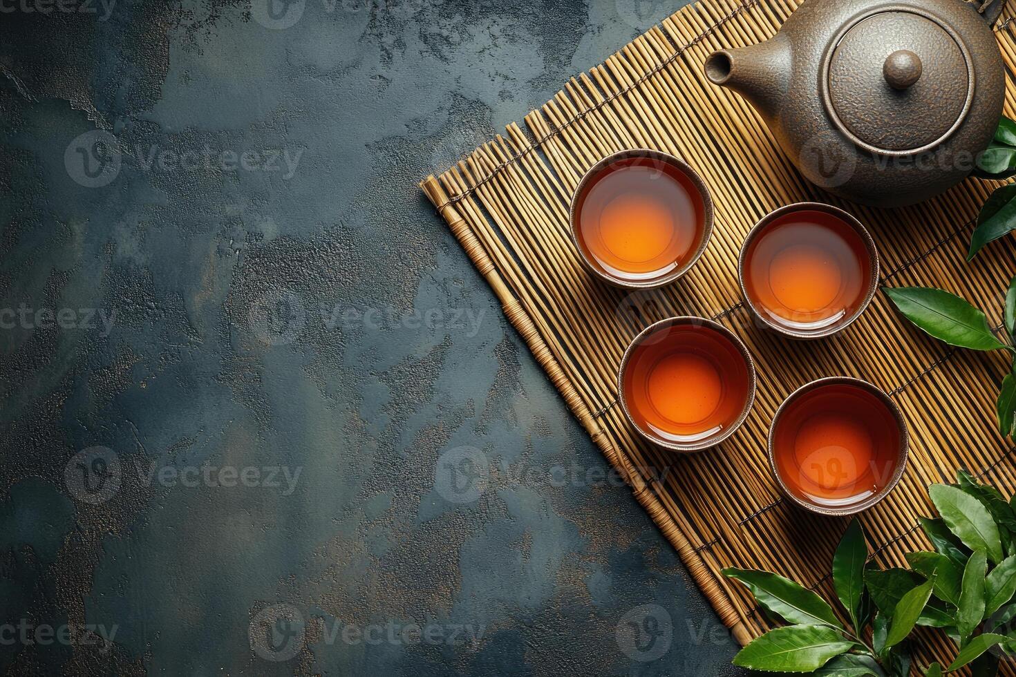 Tea ceremony composition with teapot and four cups on bamboo mat photo
